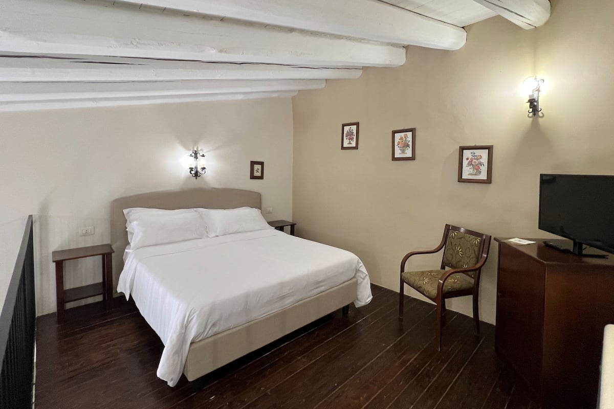 Une chambre à coucher comprenant un lit, des tables de chevet, une chaise, un bureau avec un ordinateur et des lampes fixées au mur.