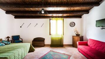 A room with a wooden ceiling, a bed with a green bedspread, a red sofa, a small wooden cabinet, and a television on the wall.