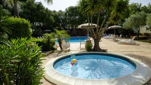 Una piscina con sillones de descanso y sombrillas, rodeada de vegetación.