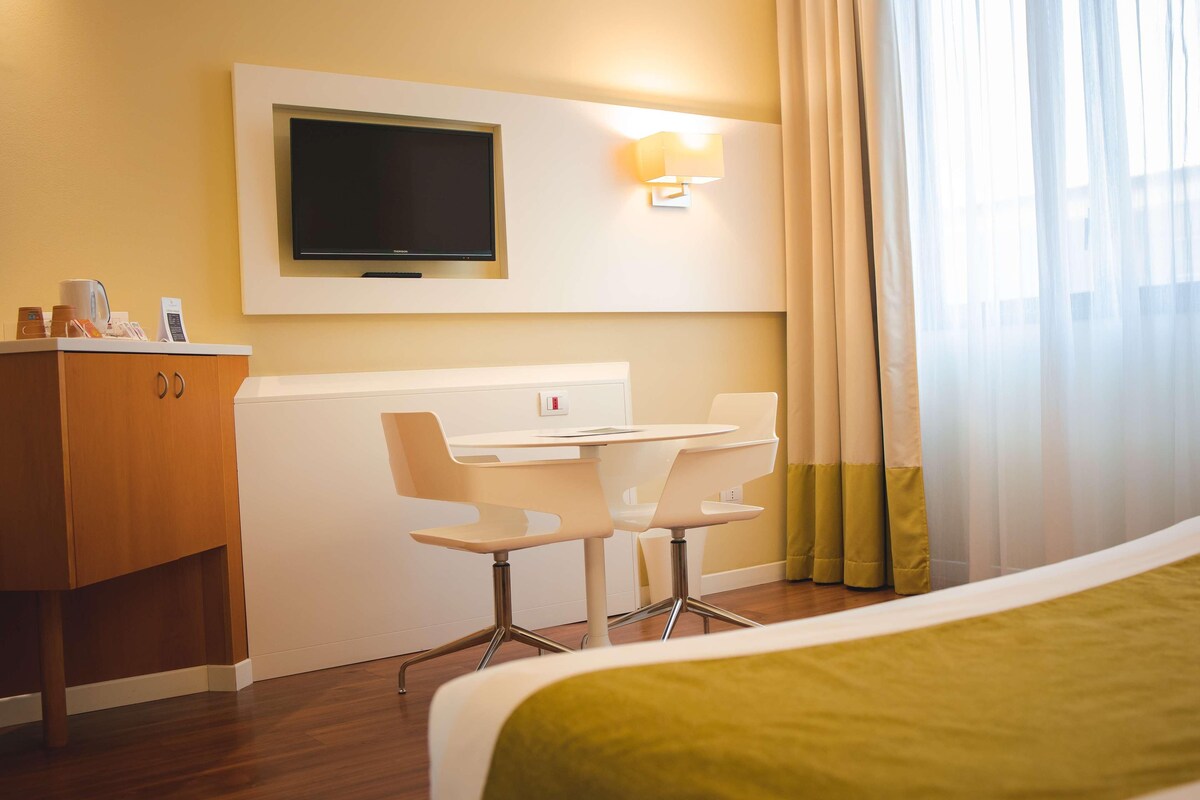 A hotel room with a bed, a desk with two chairs, a television, and a minibar.