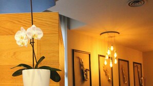 A modern living room with a white vase of orchids, wooden paneling, a sofa, and framed artwork on the wall.