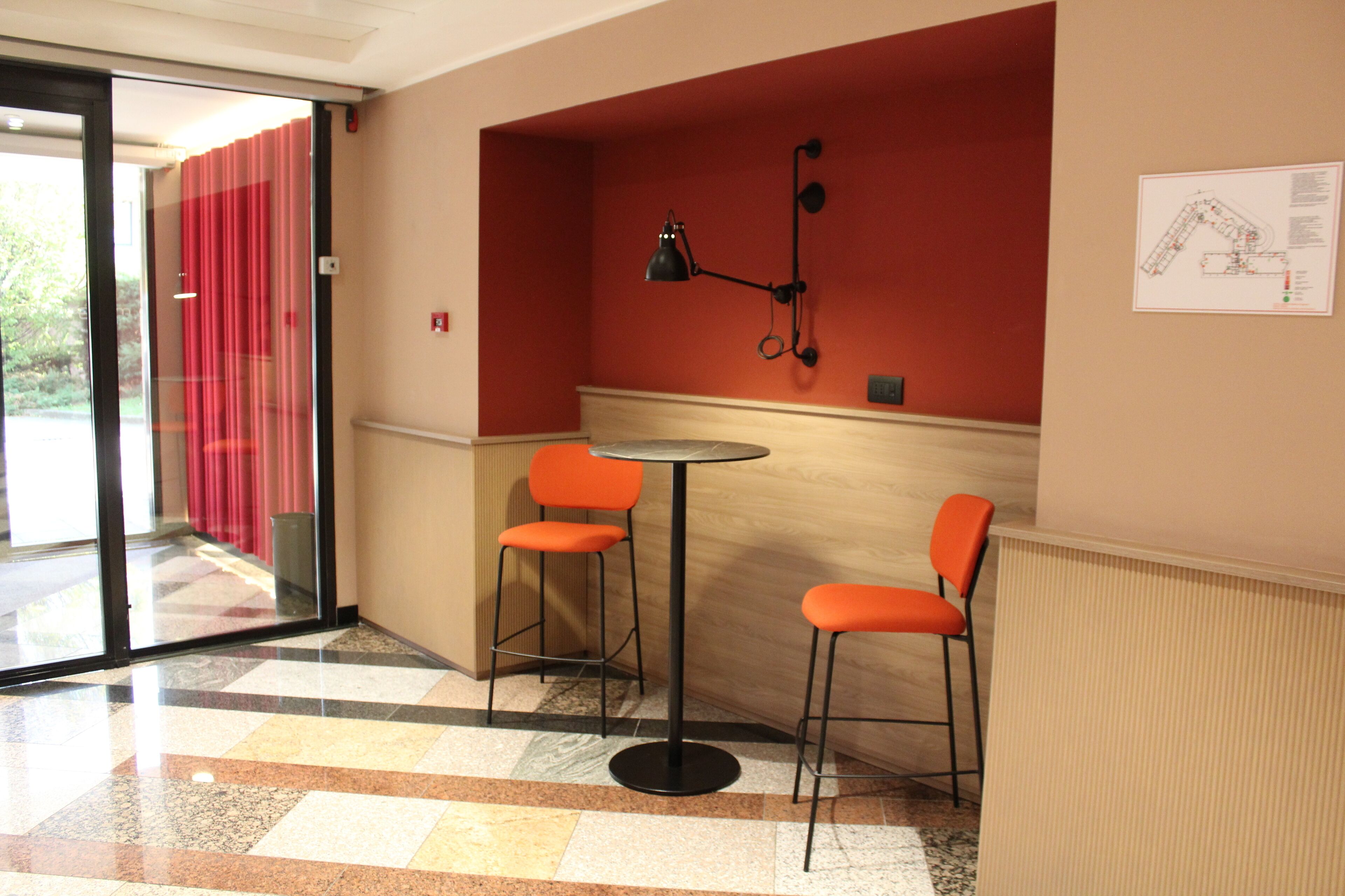 Una piccola zona con posti a sedere, due sedie, un tavolo, un muro rosso e un pavimento a scacchi.