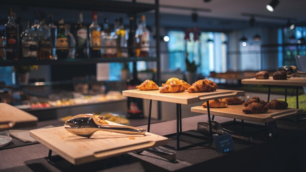 A bar area with shelves of liquor bottles, tables with croissants, and a sign indicating a croissant menu.