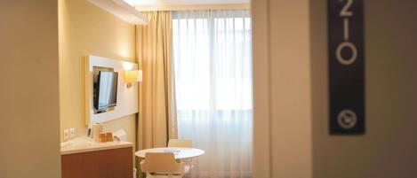 Una habitación de hotel con escritorio, silla y televisor montado en la pared.