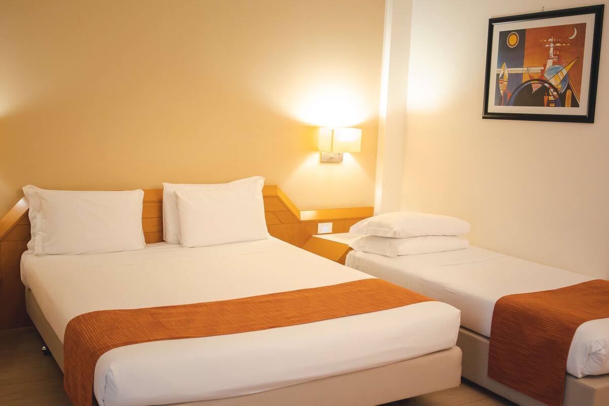 Een hotelkamer met twee bedden, een nachtkastje, een lamp en een lijst aan de muur.