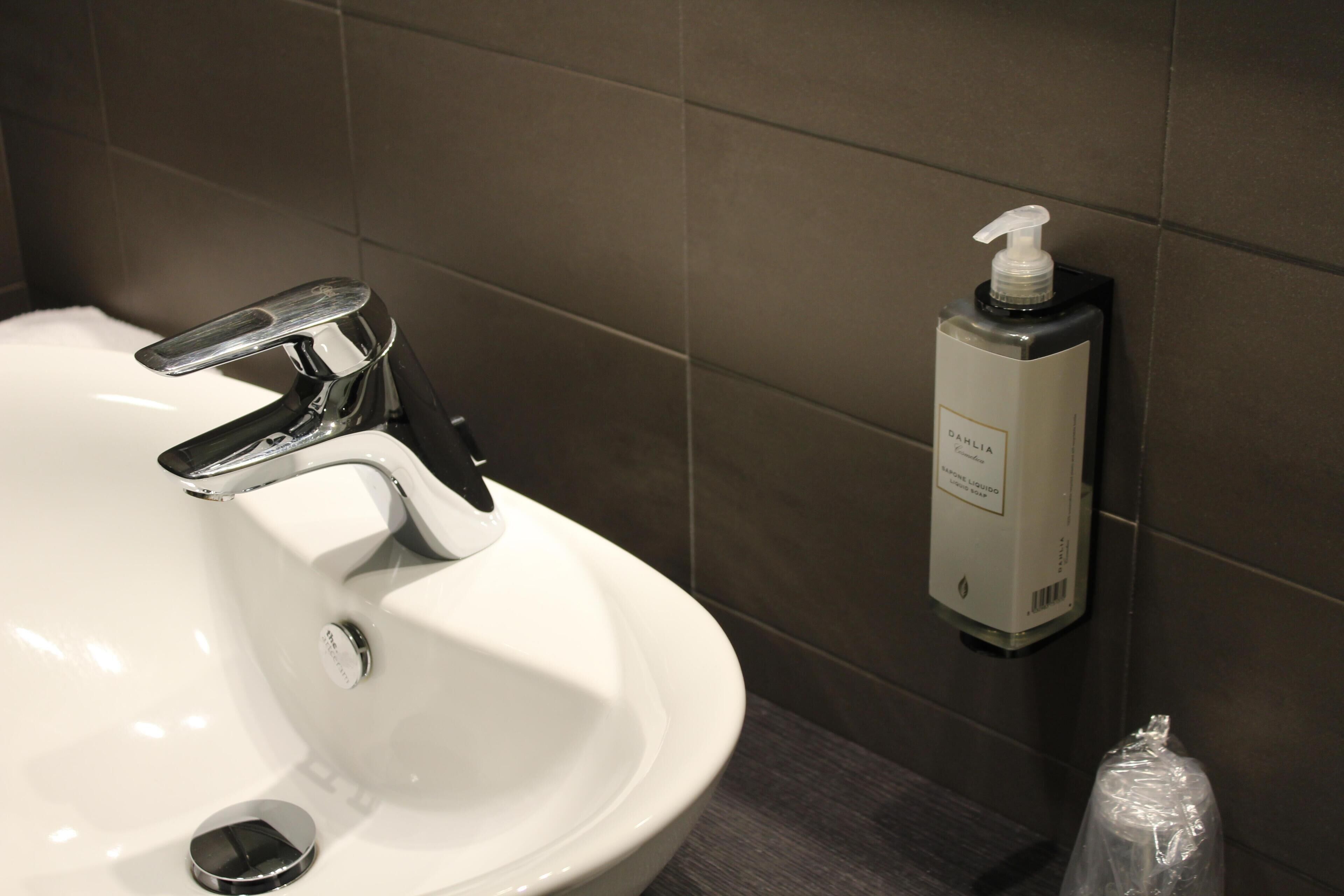 A bathroom sink with a chrome faucet and a soap dispenser mounted on the wall.