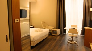 A hotel room with a bed, a chair, a small table, and a TV mounted on the wall.