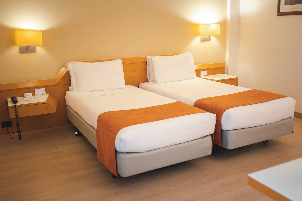 Een hotelkamer met twee bedden, een nachtkastje met een telefoon en wandlampen.