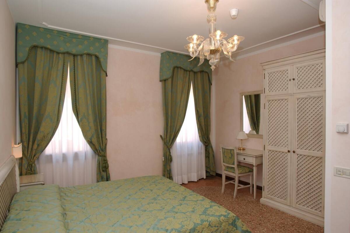 Une chambre à coucher comprenant un lit, un bureau, une chaise, une armoire et un lustre.