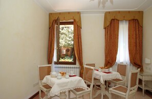 Comedor con una mesa lista para dos personas, sillas blancas y una ventana con cortinas.