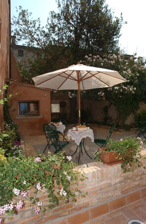 An outdoor patio with a table and chairs under a large umbrella, surrounded by brick walls and flowering plants. - Casa Mimma (Venice)