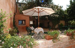 Un patio al aire libre con una mesa y sillas, rodeado de plantas y flores en macetas.