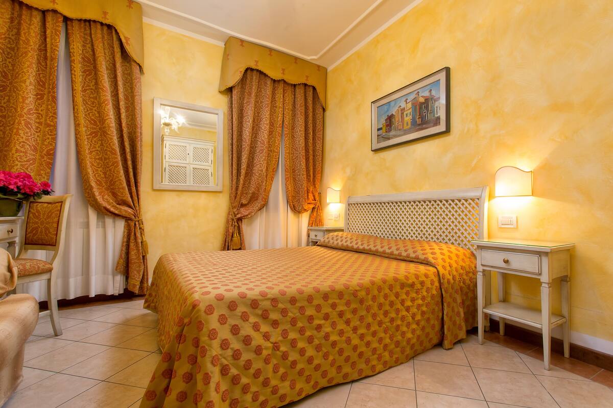 Une chambre d’hôtel avec un lit, une table de chevet, une chaise et une fenêtre avec des rideaux.