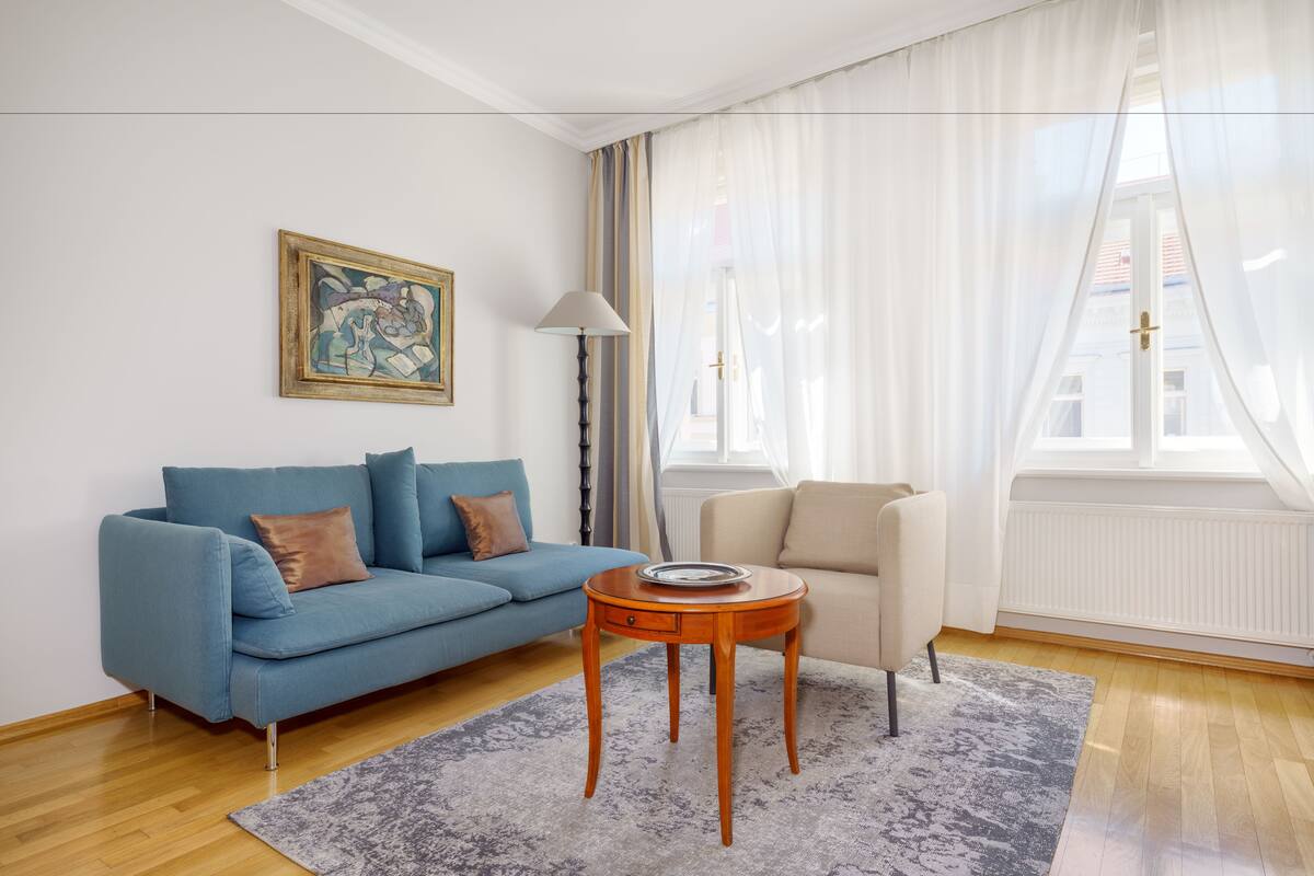Ein Wohnzimmer mit einem blauen Sofa, einem beigen Sessel, einem Holztisch und einem Gemälde an der Wand.