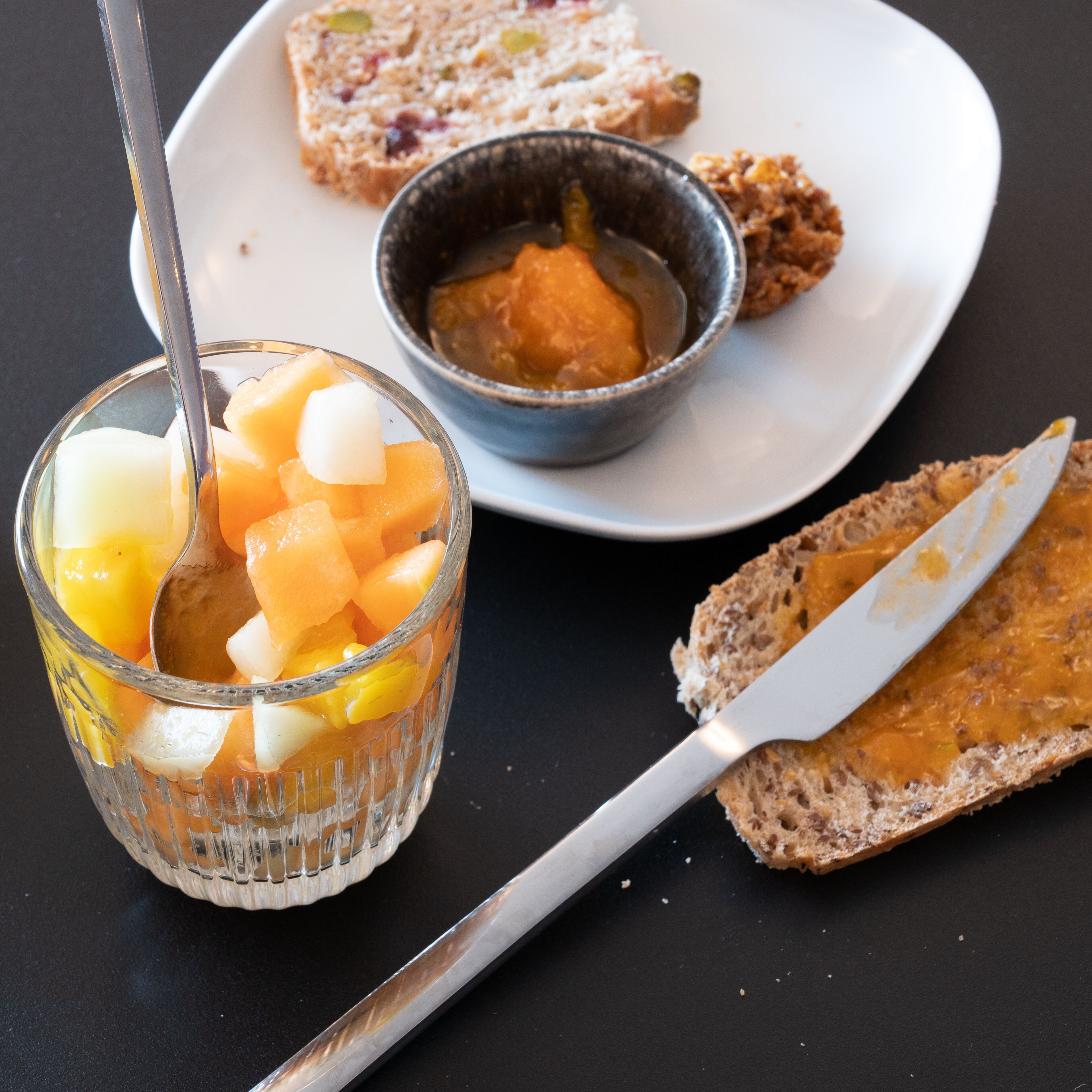 Ateria, johon kuuluu lasillinen hedelmämehua, kulho kastiketta ja viipale leipää, jossa on voita päällä, kaikki tarjoiltuna lautasella.