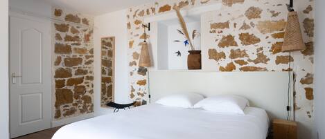 Ein Schlafzimmer mit einem großen Bett, einer Steinsäule, einem Holznachttisch und einer hängenden Leuchte.