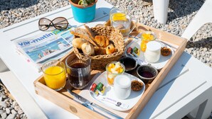 A breakfast tray with croissants, orange juice, coffee, and jam on a white table.