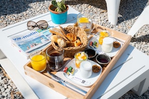 A breakfast tray with croissants, orange juice, coffee, and jam on a white table.