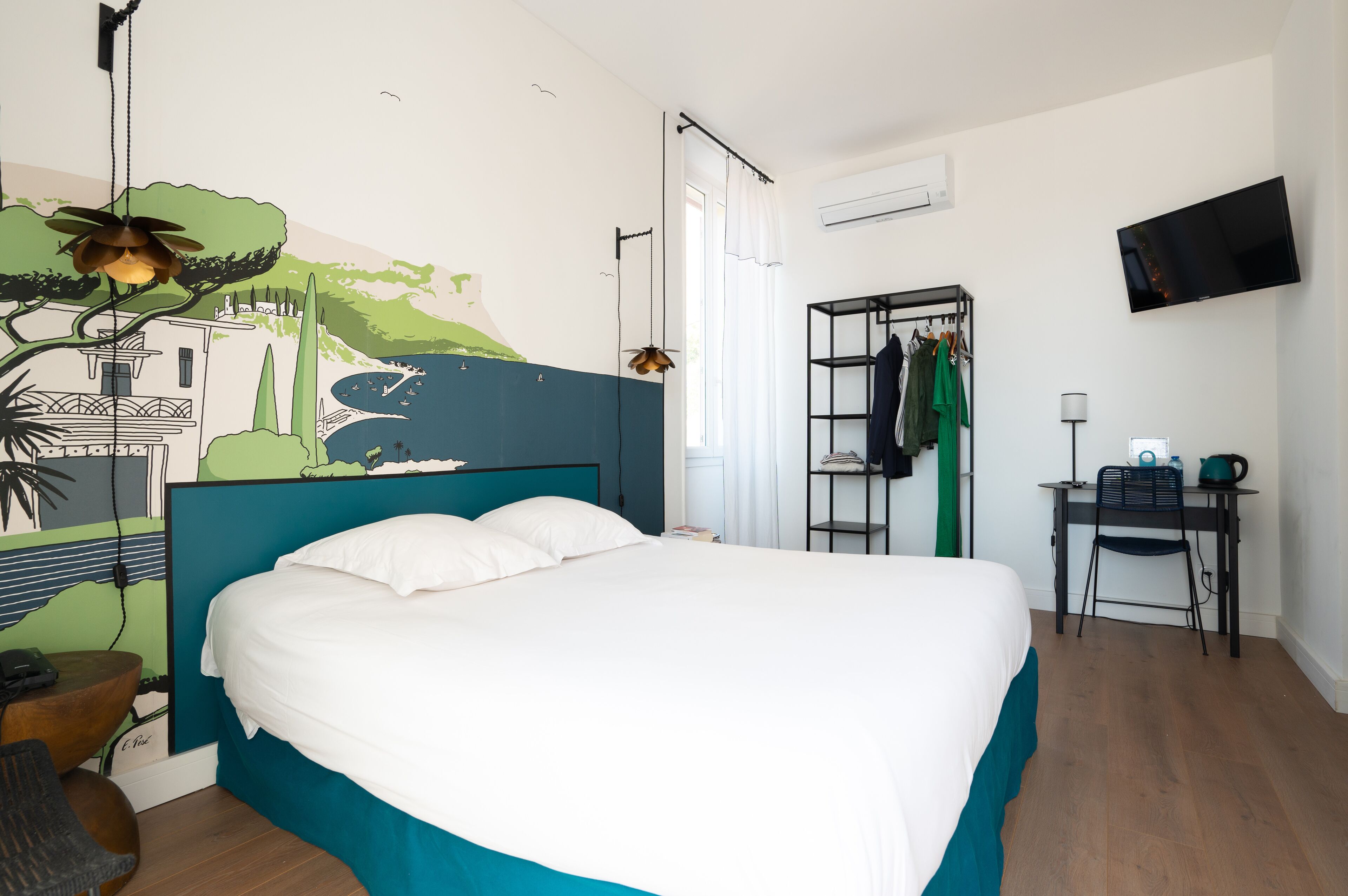 A bedroom with a bed, a desk, a chair, a TV, and a wall with a mural.