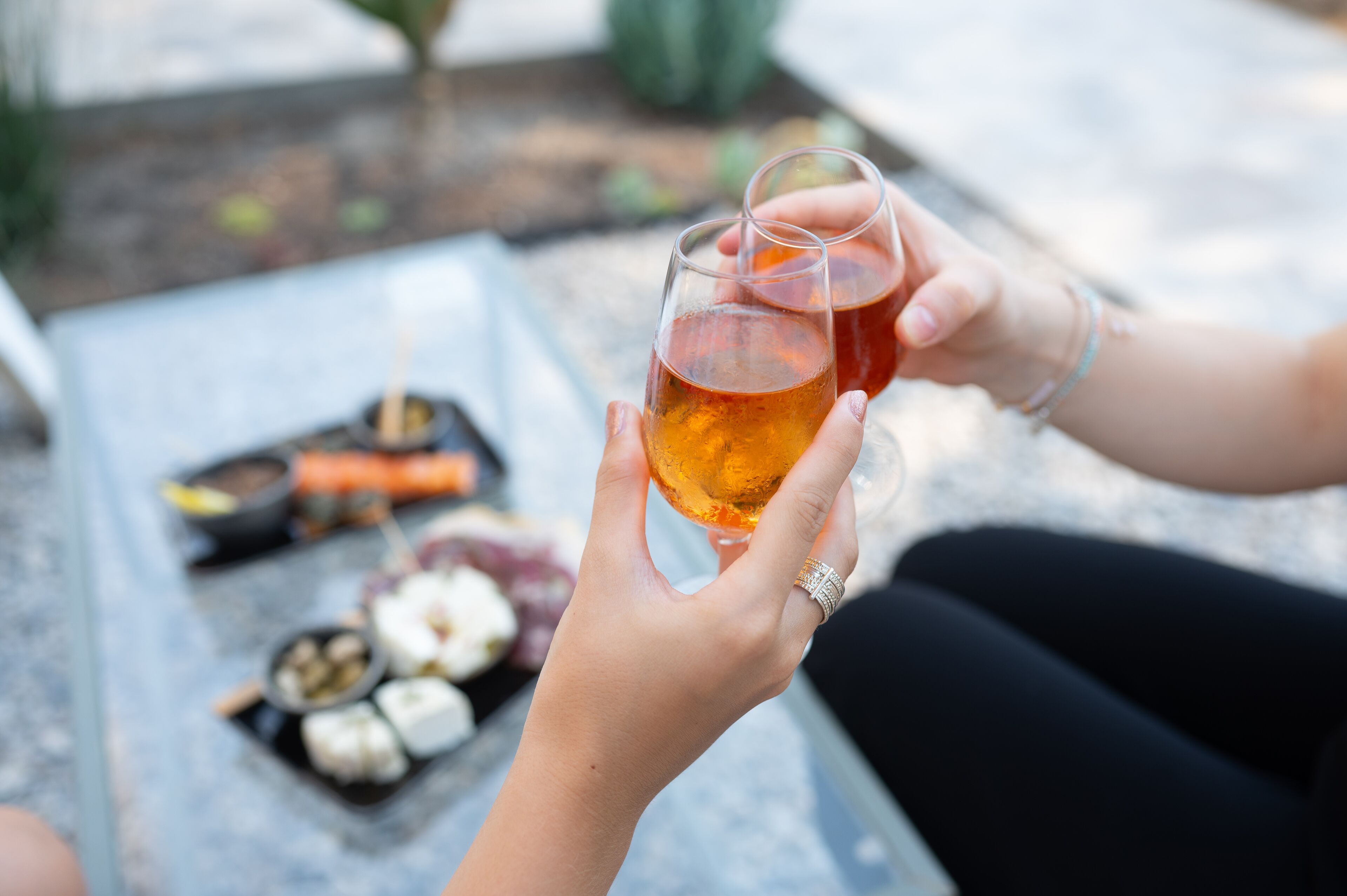 Eine Person hält ein Glas mit bernsteinfarbiger Flüssigkeit, möglicherweise Tee, im Hintergrund steht ein Teller mit Speisen.