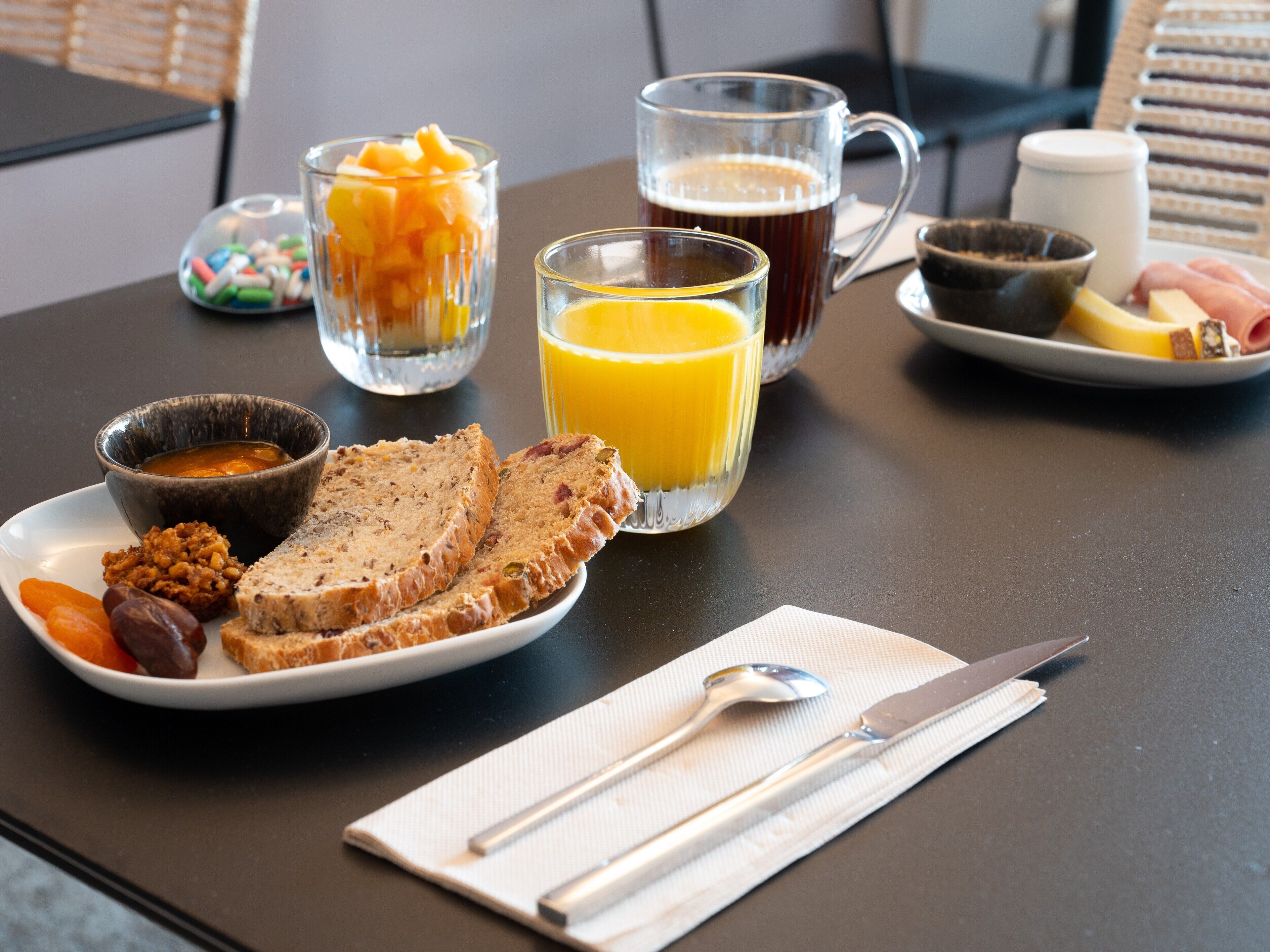 Una mesa con pan, fruta, una taza de café y un vaso de zumo de naranja.