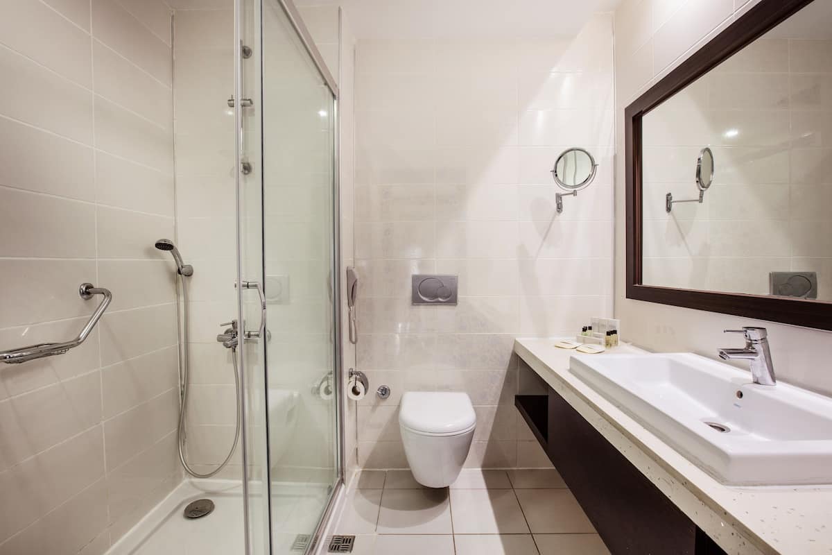 A modern bathroom with a glass shower enclosure, a white toilet, and a large sink with a mirror.