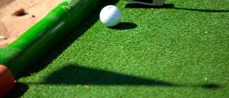 Primer plano de un taco golpeando una bola de golf blanca sobre una superficie de fieltro verde.