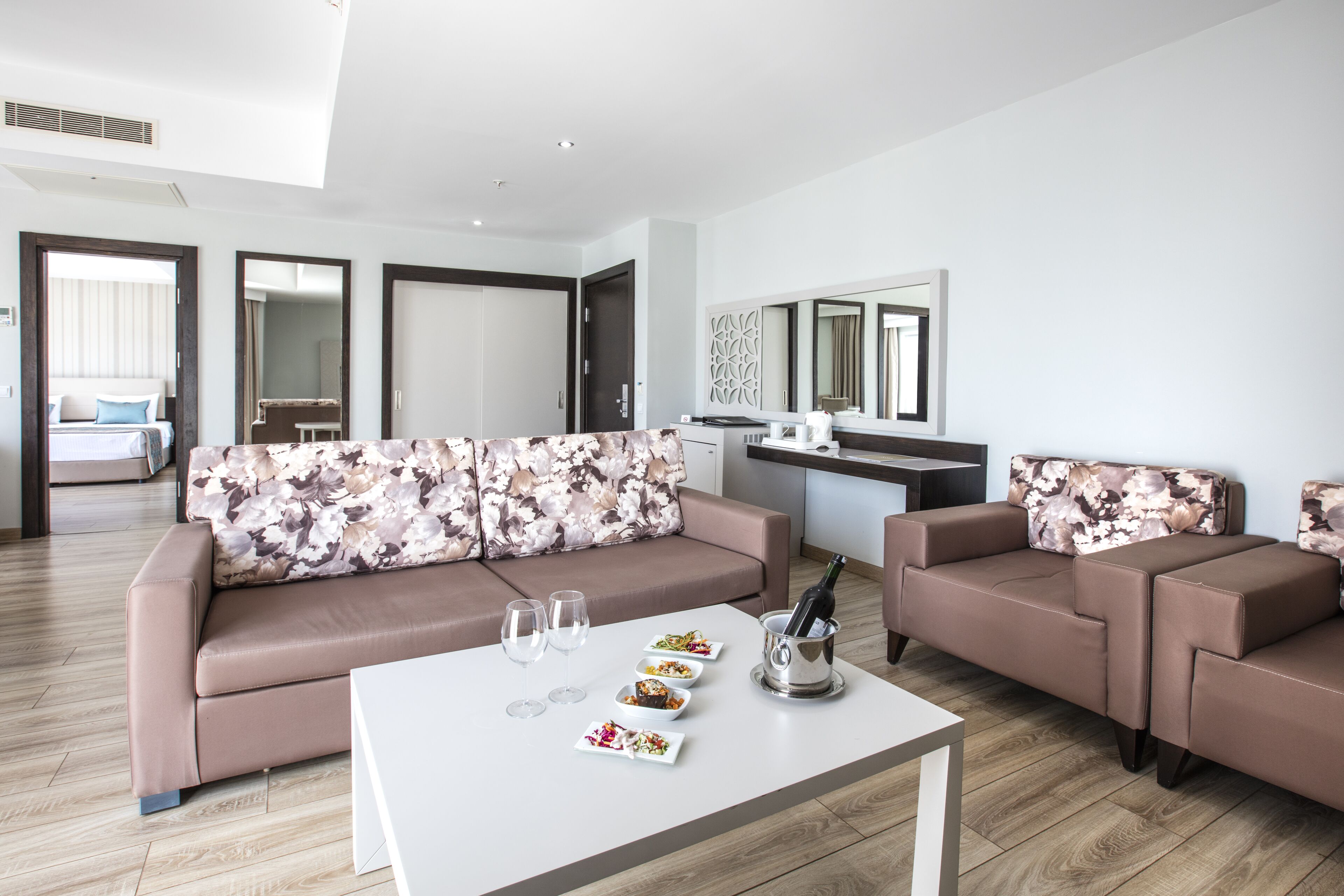 A modern living room with a sofa, a coffee table with food and drinks, and a kitchen area in the background.