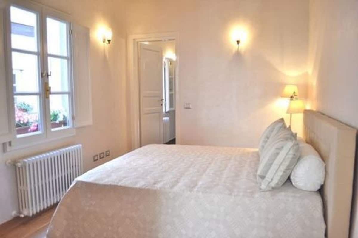 A bedroom with a bed, a window, and two wall-mounted lamps.