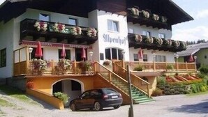 A hotel with a traditional Alpine architectural style, featuring a balcony with floral decorations and a staircase leading to the entrance. - Alpenhof (Sankt Martin am Tennengebirge)