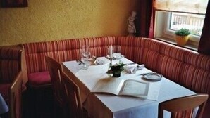 A dining area with a booth seating arrangement, a table set for two, and a window with a view. - Alpenhof (Sankt Martin am Tennengebirge)