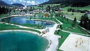 A lakeside village with a church, houses, and a large pond. - Alpenhof (Sankt Martin am Tennengebirge)