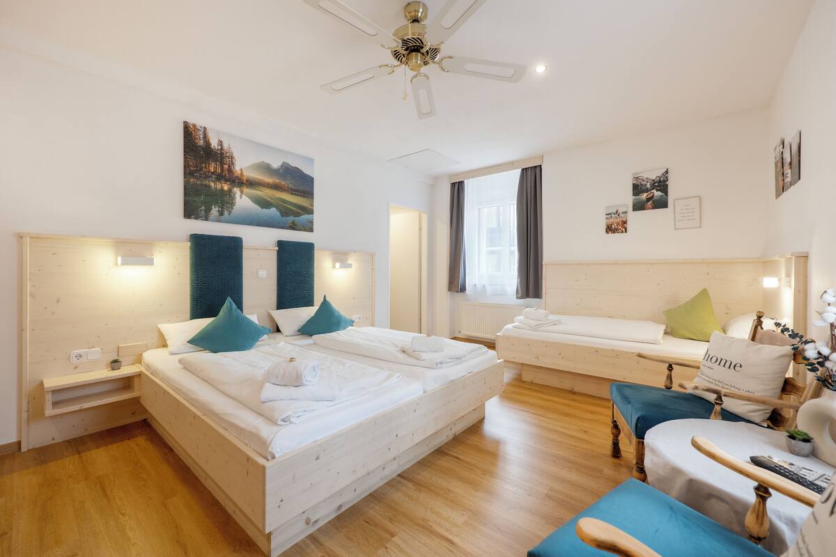 A hotel room with two beds, a sofa, a chair, a ceiling fan, and artwork on the walls.