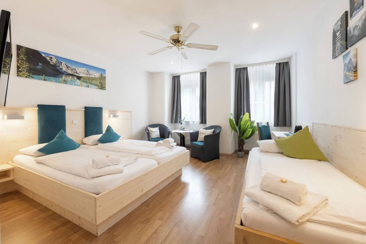 A hotel room with two beds, a desk, a chair, a ceiling fan, and a painting on the wall.