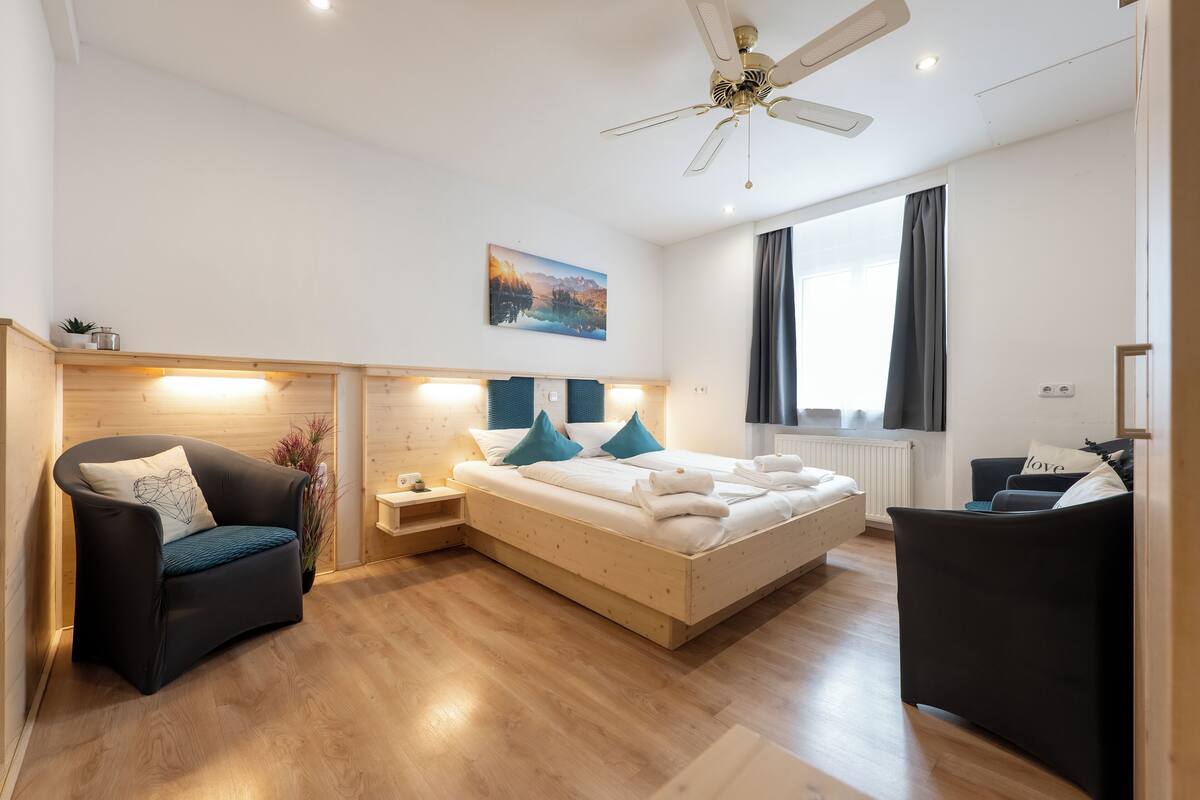 A modern bedroom with a bed, a chair, a desk, and a ceiling fan.