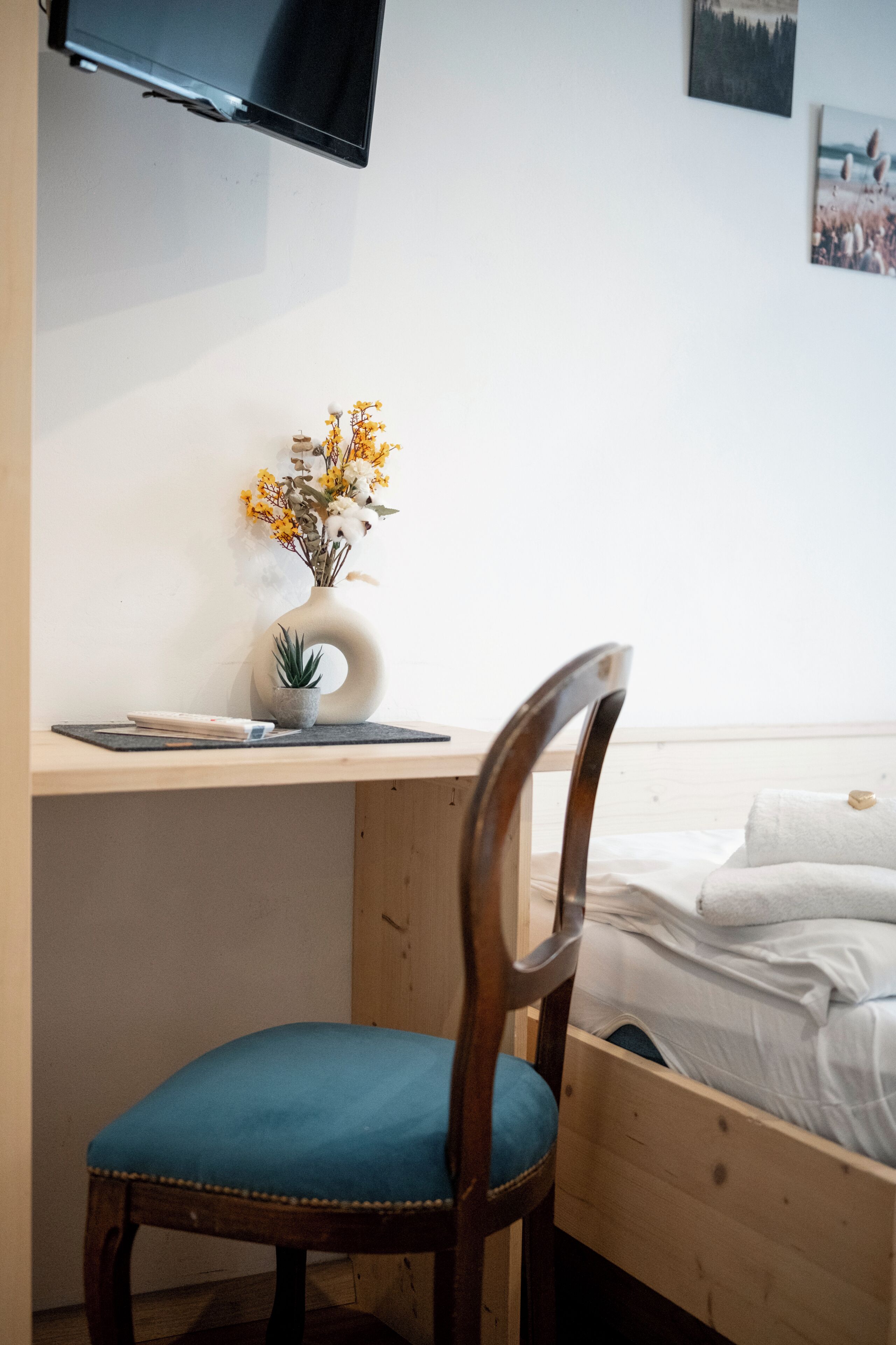 Een kamer met een houten bureau, een stoel, een bed en een tv aan de muur.