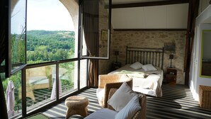 Een slaapkamer met een groot rondboogvenster, een bed, een nachtkastje en rieten meubels.
