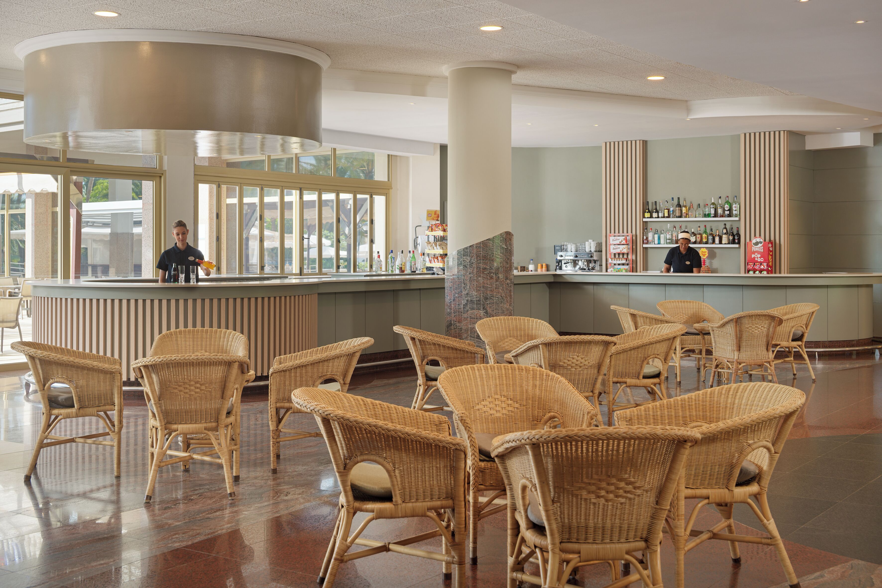 Zona de bar con sillas de mimbre, una barra y estantes con botellas.