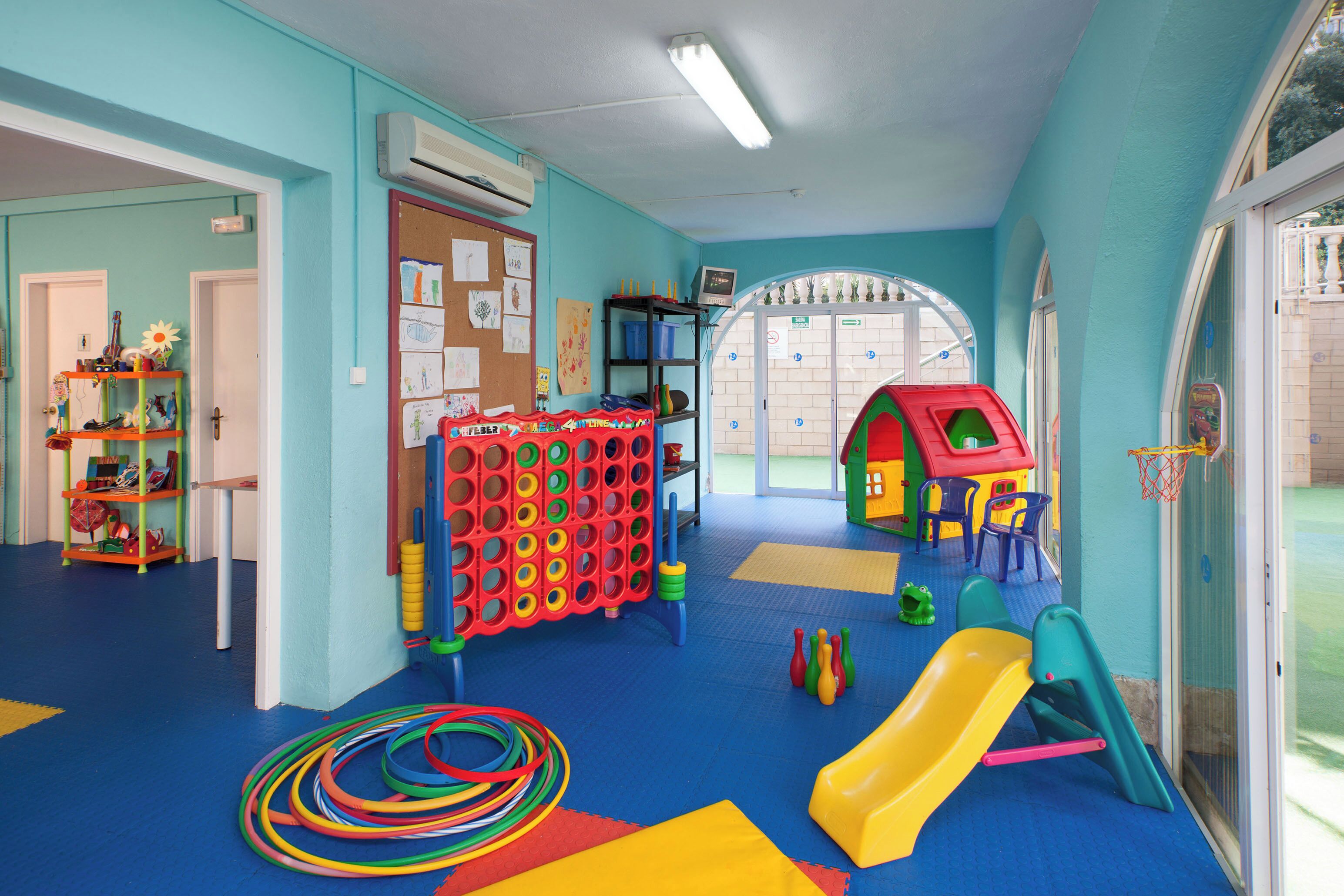 Un área de juegos interior, llena de color, con un tobogán, túneles de juego y diversos juguetes.