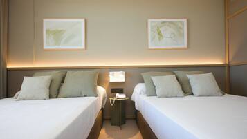 Habitación de hotel con dos camas, cada una con ropa blanca y almohadas verdes. Dos cuadros enmarcados decoran la pared sobre las camas.