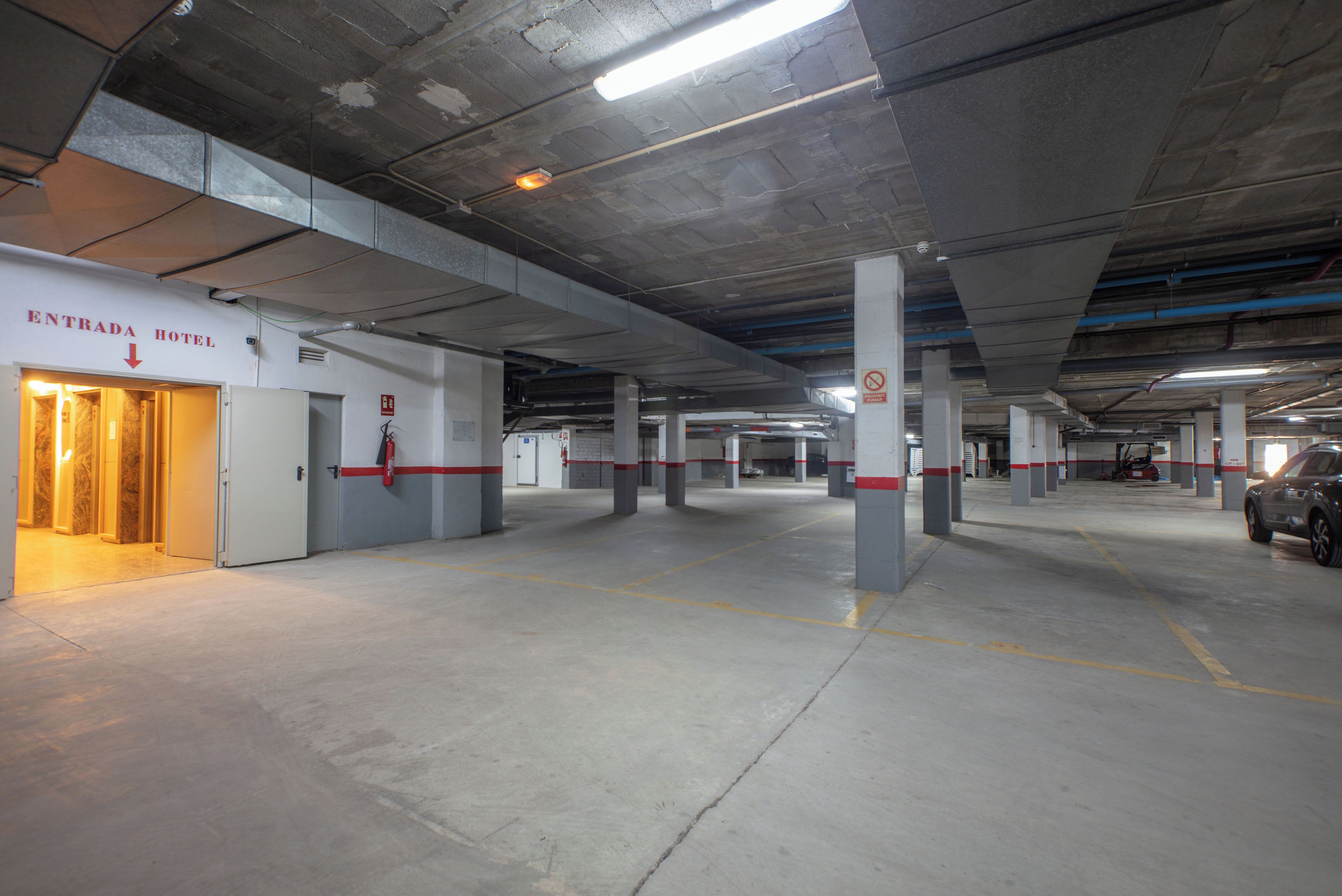 Un parking souterrain doté de nombreuses places de stationnement, de piliers en béton et d’une entrée d’hôtel signalée par l’inscription « ENTRADA HOTEL ».