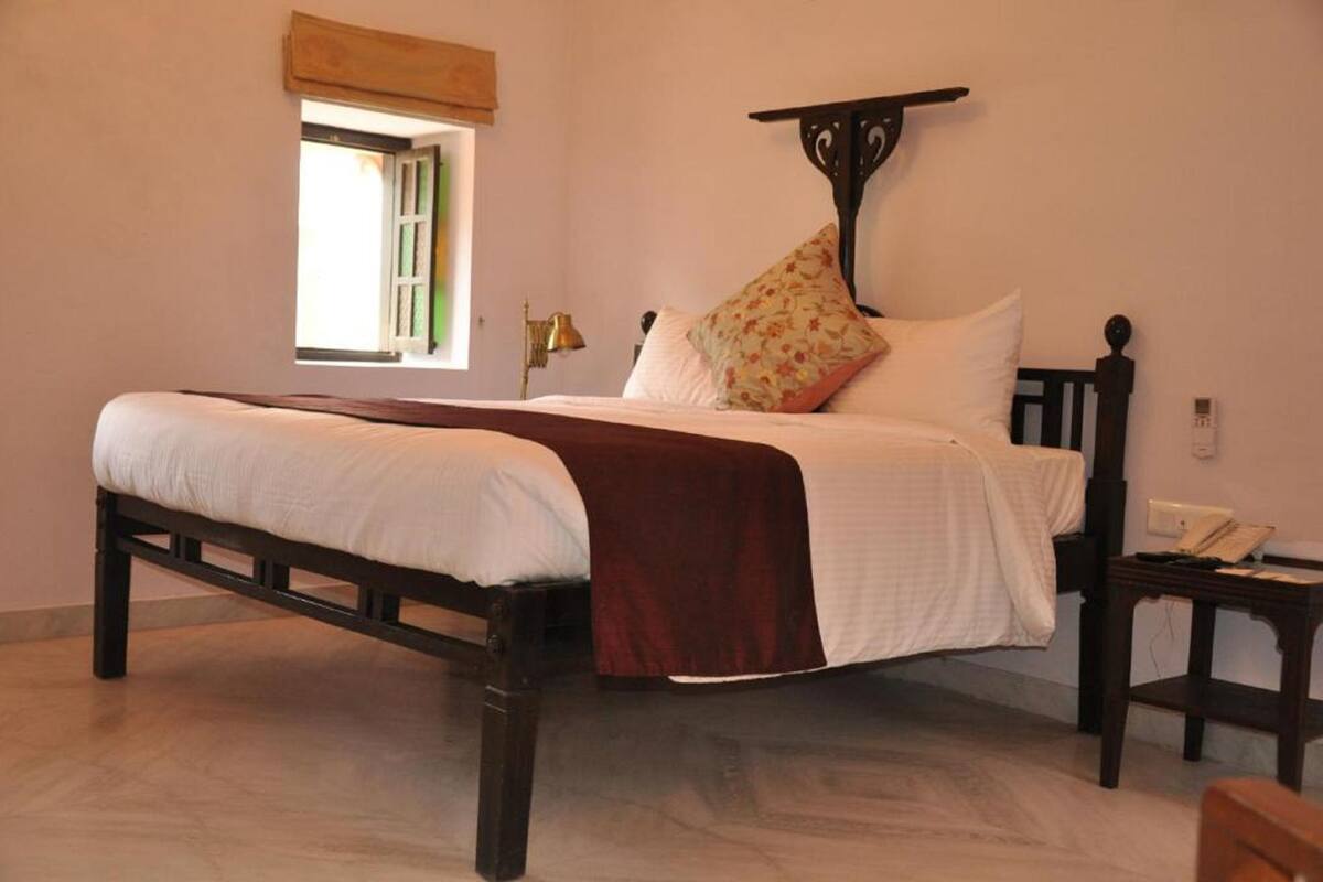 Uma cama com cabeceira, mesa de cabeceira, luminária e janela com vista.