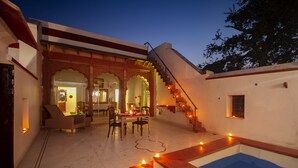 A traditional building with a pool, a staircase, and a dining area with chairs and a table. - Amritara Chandra Mahal Haveli (Nadbai)