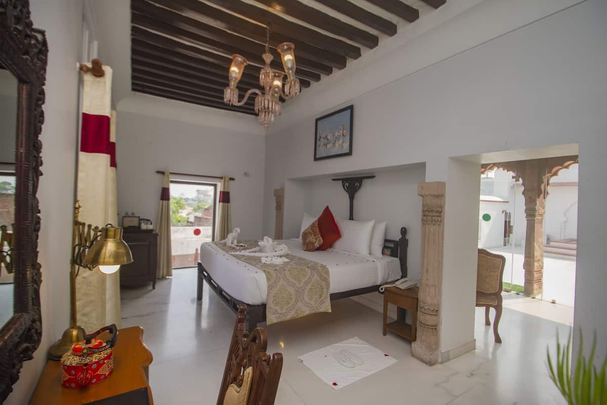Quarto com cama, escrivaninha, cadeira, lustre e vista para o exterior.