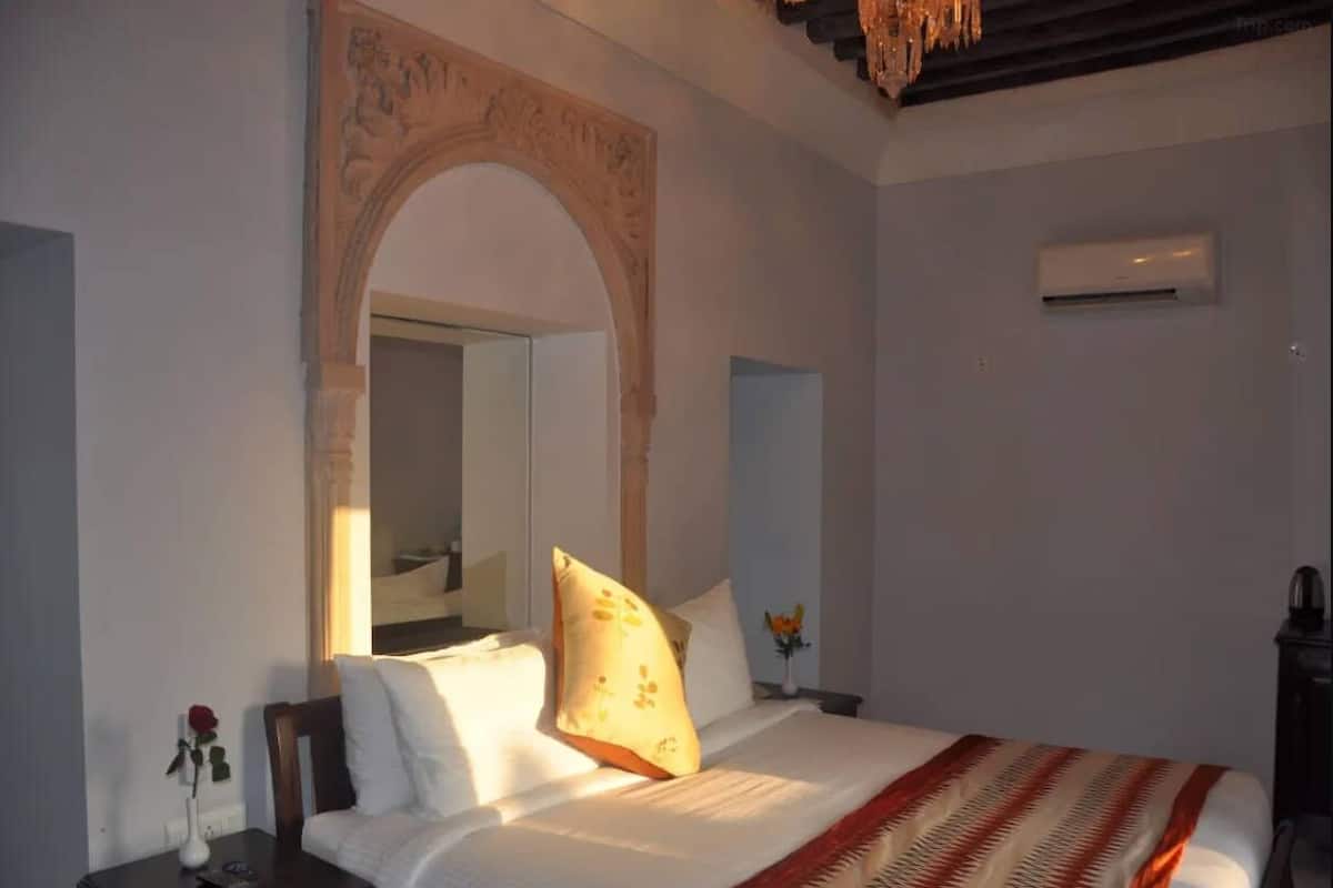 Quarto com cama, mesa de cabeceira, espelho e porta em arco.