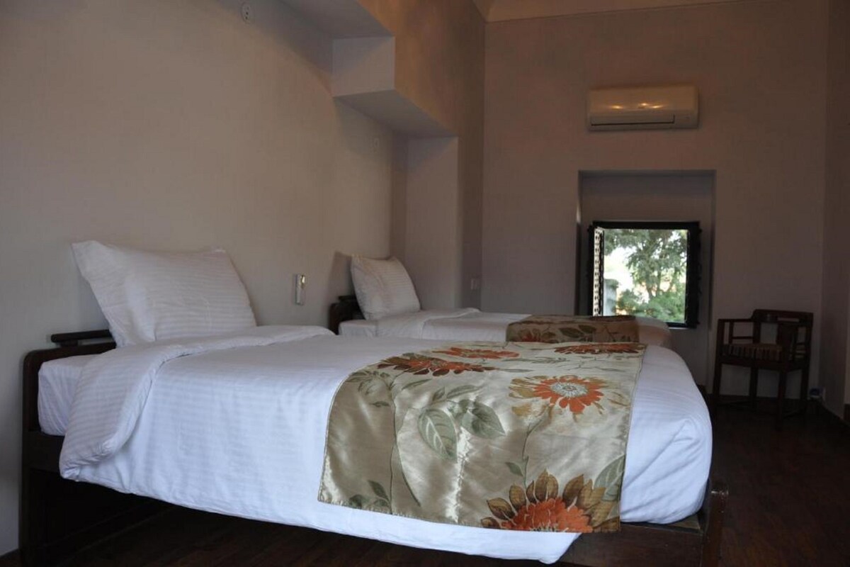 A bedroom with a large bed, two pillows, a floral bedspread, a window, and an air conditioning unit.