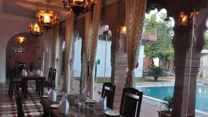 A dining area with tables set for service, a pool visible through the windows, and a chandelier hanging from the ceiling. - Amritara Chandra Mahal Haveli (Nadbai)
