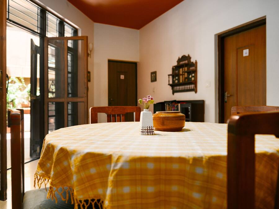 Un área de comedor con una mesa lista para dos personas, un florero con flores y un armario de madera.