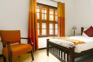 A bedroom with a wooden bed, a chair, a window with curtains, and a bedside lamp.