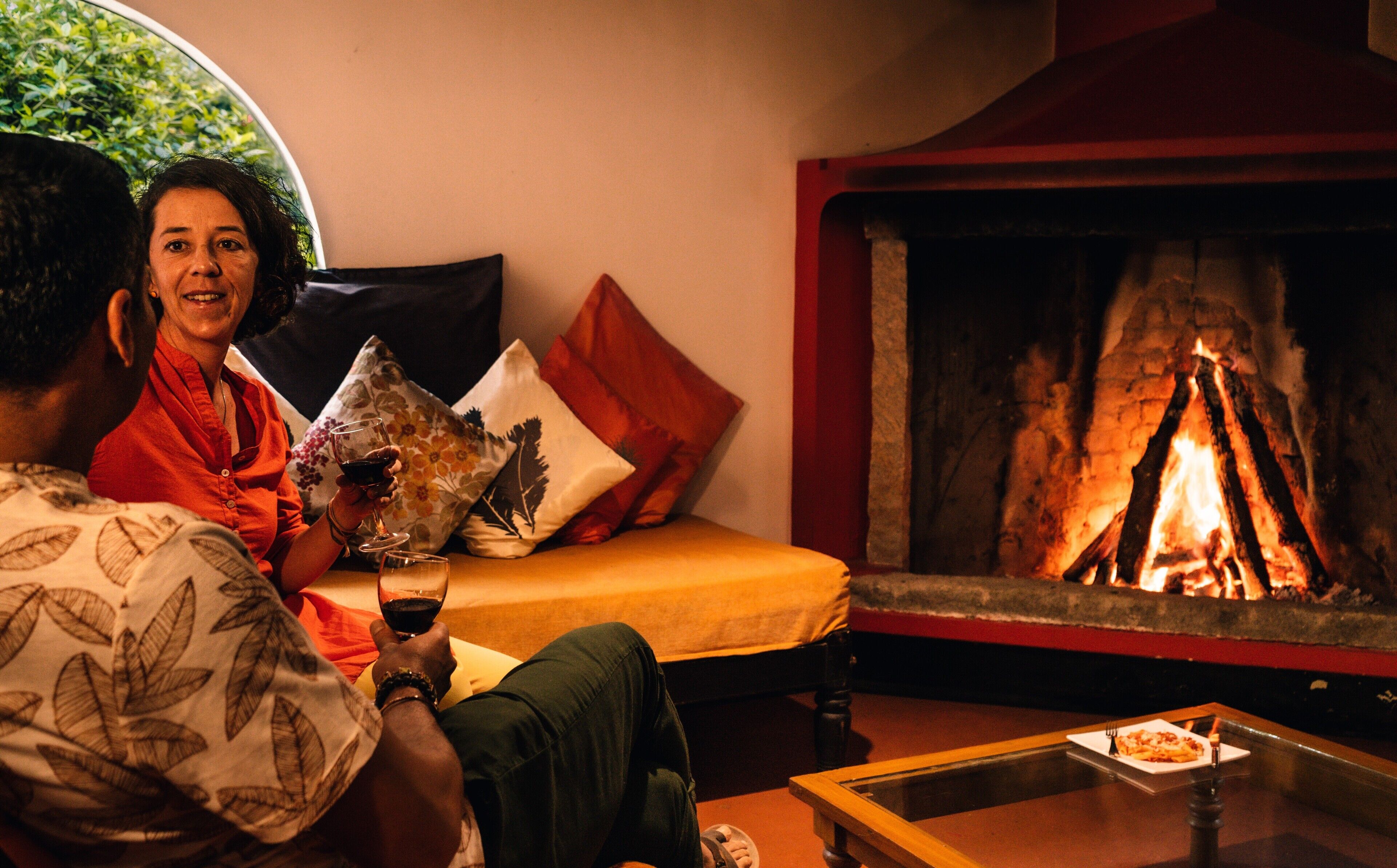 A cozy living room with a fireplace, a sofa with cushions, and a glass of wine on a table.